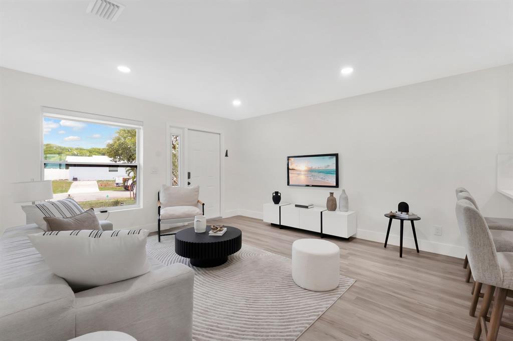 A bright living room features light wood-look flooring, a white sofa, and a wall-mounted television — 1115 Stillwater Drive, Jupiter FL 33458, JUPITER, FL