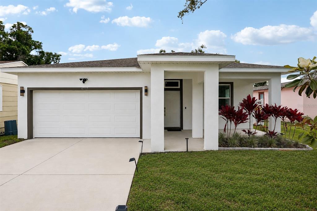 A white single-story house with a garage, front porch, and red tropical plants — 4277 43RD AVENUE N, ST PETERSBURG, FL