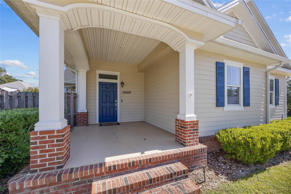 A covered front porch features brick pillars, a blue door, and light-colored horizontal siding — 16609 NW 166TH DRIVE, ALACHUA, FL
