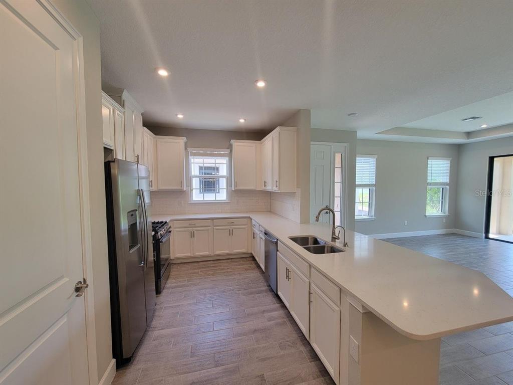 A kitchen with white cabinets, stainless steel appliances, and a long quartz-topped island — 5331 RUSHMERE COURT, PALMETTO, FL