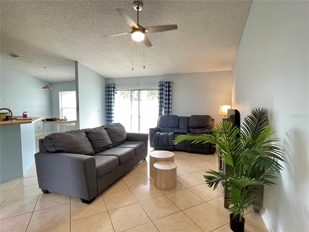 A living room features a gray sofa, a dark loveseat, tile flooring, and a ceiling fan — 1150 INDIAN RIDGE TRAIL E, KISSIMMEE, FL