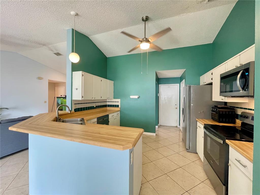 A kitchen with teal walls, white cabinets, wood-look countertops, and a ceiling fan — 1150 INDIAN RIDGE TRAIL E, KISSIMMEE, FL