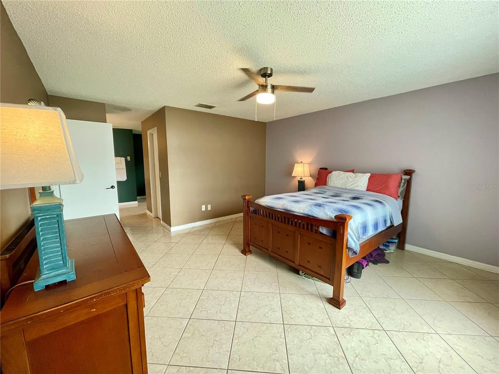 A bedroom features a wooden bed frame, tile flooring, and a ceiling fan — 1150 INDIAN RIDGE TRAIL E, KISSIMMEE, FL