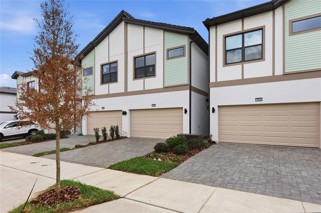 A row of modern townhouses with beige garage doors and light-colored siding under a blue sky — 10556 EBB TIDE LANE, ORLANDO, FL