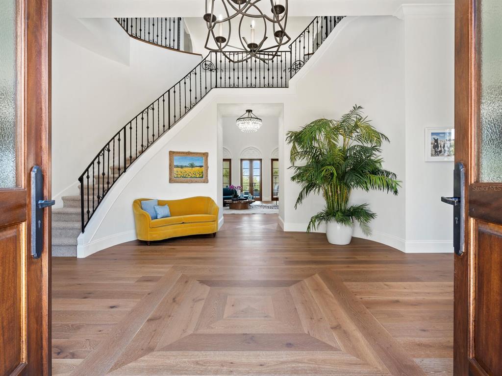 A bright foyer features hardwood floors, a curved staircase, a yellow sofa, and a chandelier — 4205 HIGEL AVENUE, SARASOTA, FL