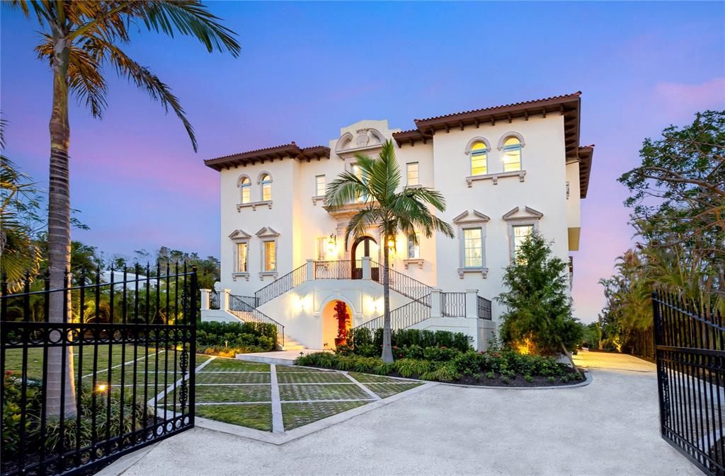 A large, multi-story Mediterranean-style mansion with a grand staircase and gated driveway at dusk — 4205 HIGEL AVENUE, SARASOTA, FL
