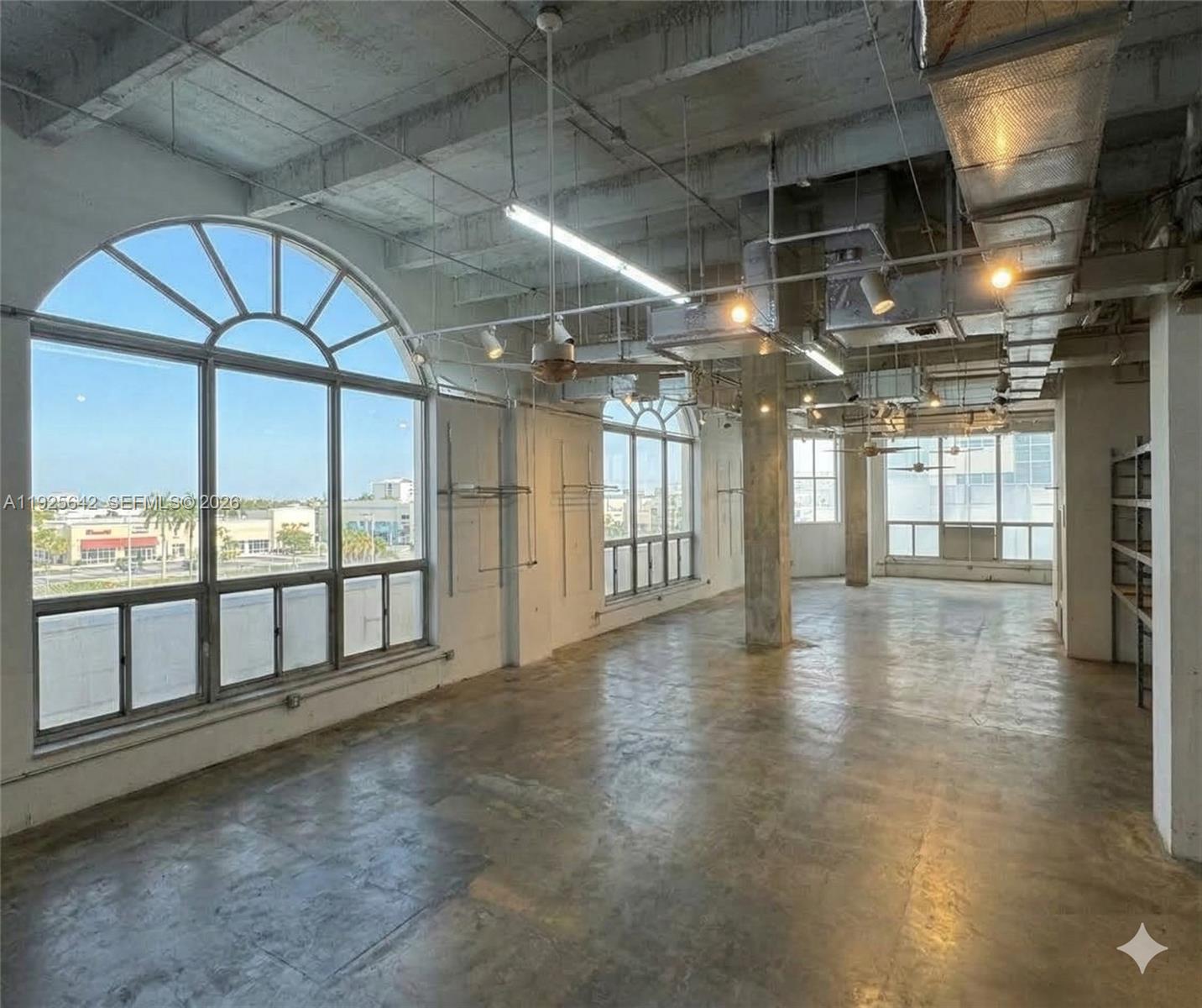 An industrial-style open room features concrete floors, exposed ductwork, and large arched windows — 2801 BISCAYNE BLVD, Miami FL 33137, MIAMI, FL