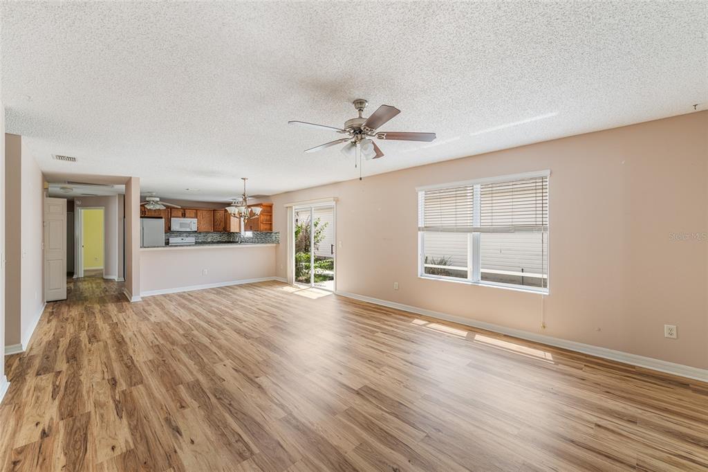 An open-concept living area with wood-look flooring, a ceiling fan, and an adjacent kitchen — 8932 SE 168TH SEDGWICK PLACE, THE VILLAGES, FL