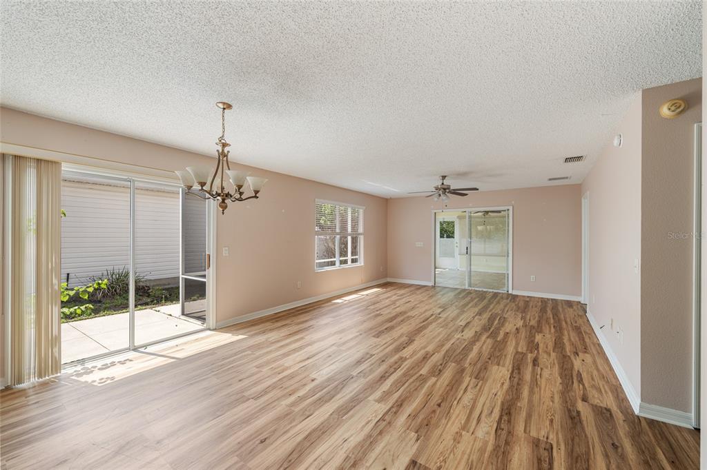 A spacious living room features light-colored walls, wood-look flooring, a ceiling fan, and sliding doors — 8932 SE 168TH SEDGWICK PLACE, THE VILLAGES, FL