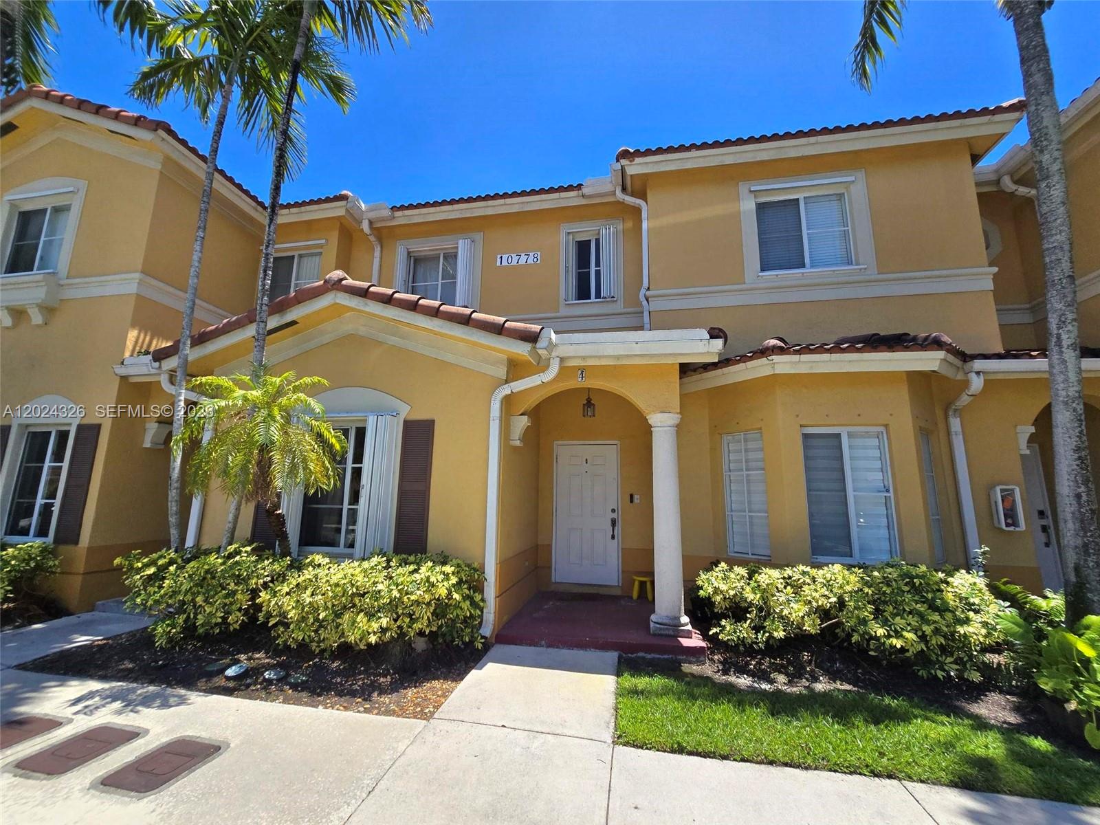 A yellow two-story townhouse features a covered entryway with a column and palm trees — 10778 NW 84th St # 27, Doral FL 33178, DORAL, FL