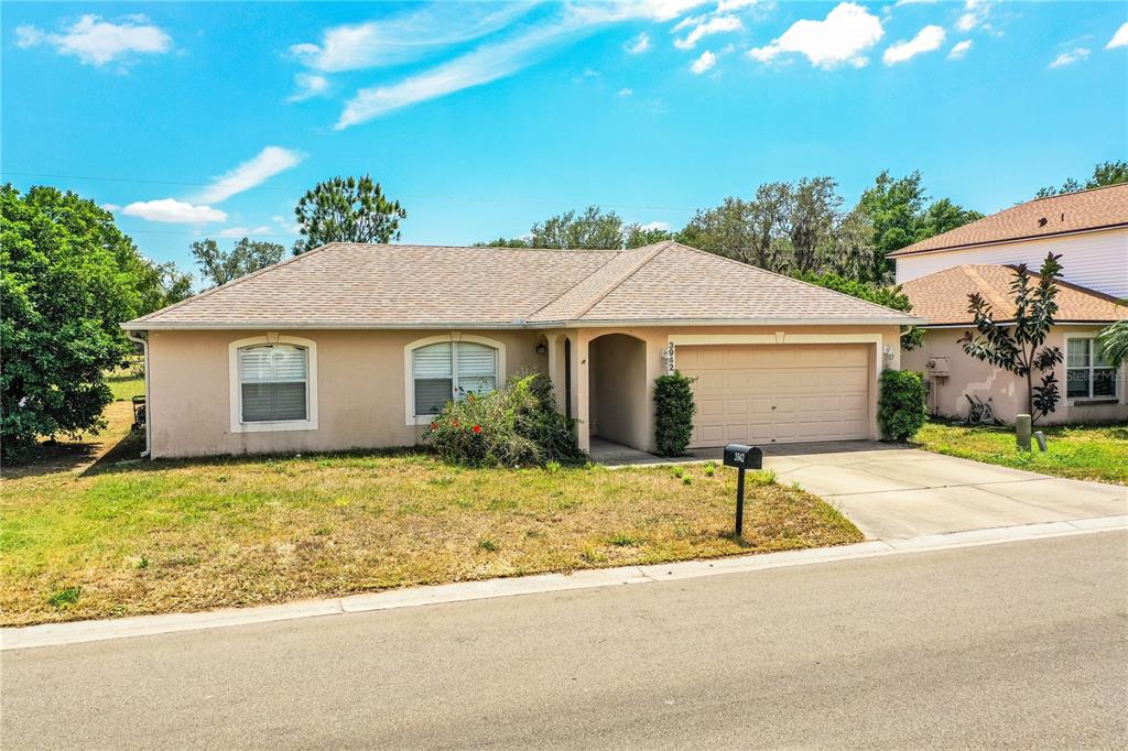 A single-story house with a tan stucco exterior, a shingled roof, and a two-car garage — 3942 WARBLER DRIVE, WINTER HAVEN, FL