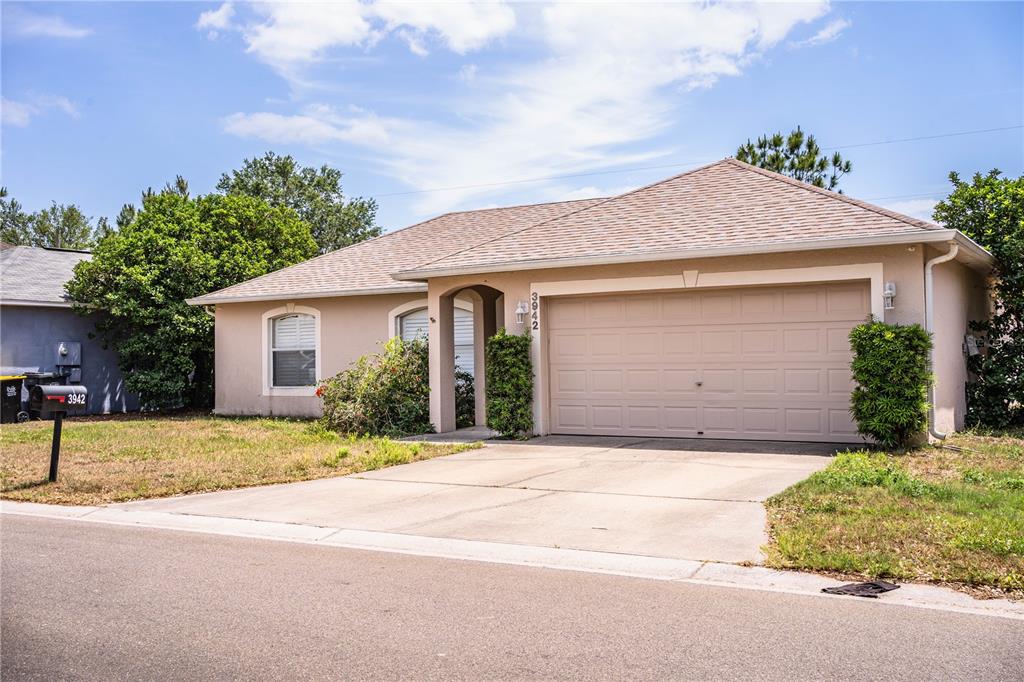 A single-story house with a beige stucco exterior, a two-car garage, and a concrete driveway — 3942 WARBLER DRIVE, WINTER HAVEN, FL