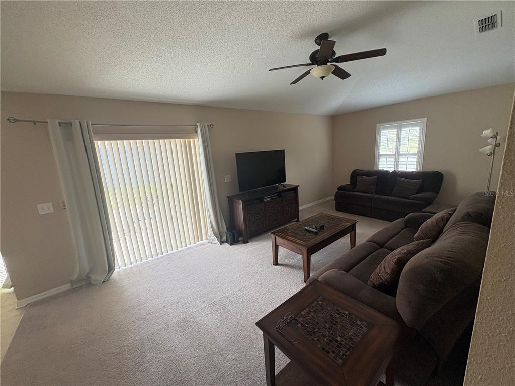 A living room features beige carpet, two brown sofas, a coffee table, and sliding glass doors — 3942 WARBLER DRIVE, WINTER HAVEN, FL