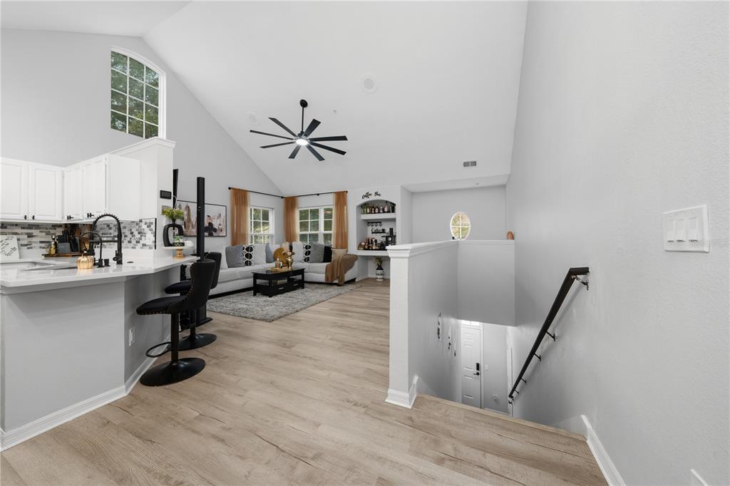 A bright open-concept living area with light wood flooring, a kitchen island, and a staircase — 3432 WESTCHESTER SQUARE BOULEVARD UNIT 203, ORLANDO, FL