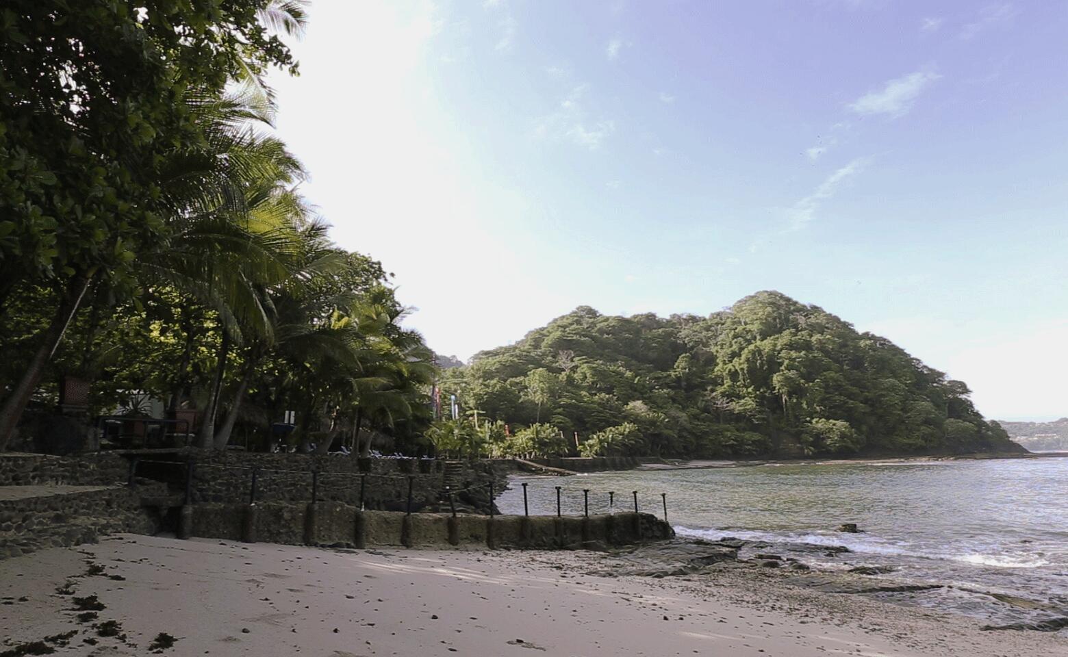 A sandy beach leads to a stone retaining wall and a lush, forested coastal hill — 0 Playa Caletas, Canton De Garabito, Puntarenas, FL