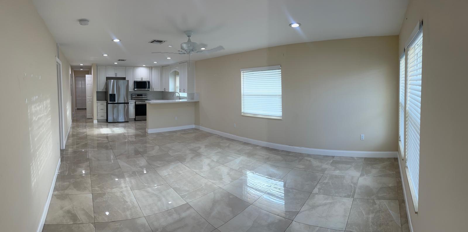 An open-concept living area with large beige floor tiles and a kitchen with white cabinets — 962 29th Street, West Palm Beach FL 33407, WEST PALM BEACH, FL