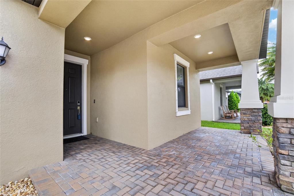A covered front porch features brick pavers, recessed lighting, and a dark front door — 9930 IVORY DRIVE, RUSKIN, FL