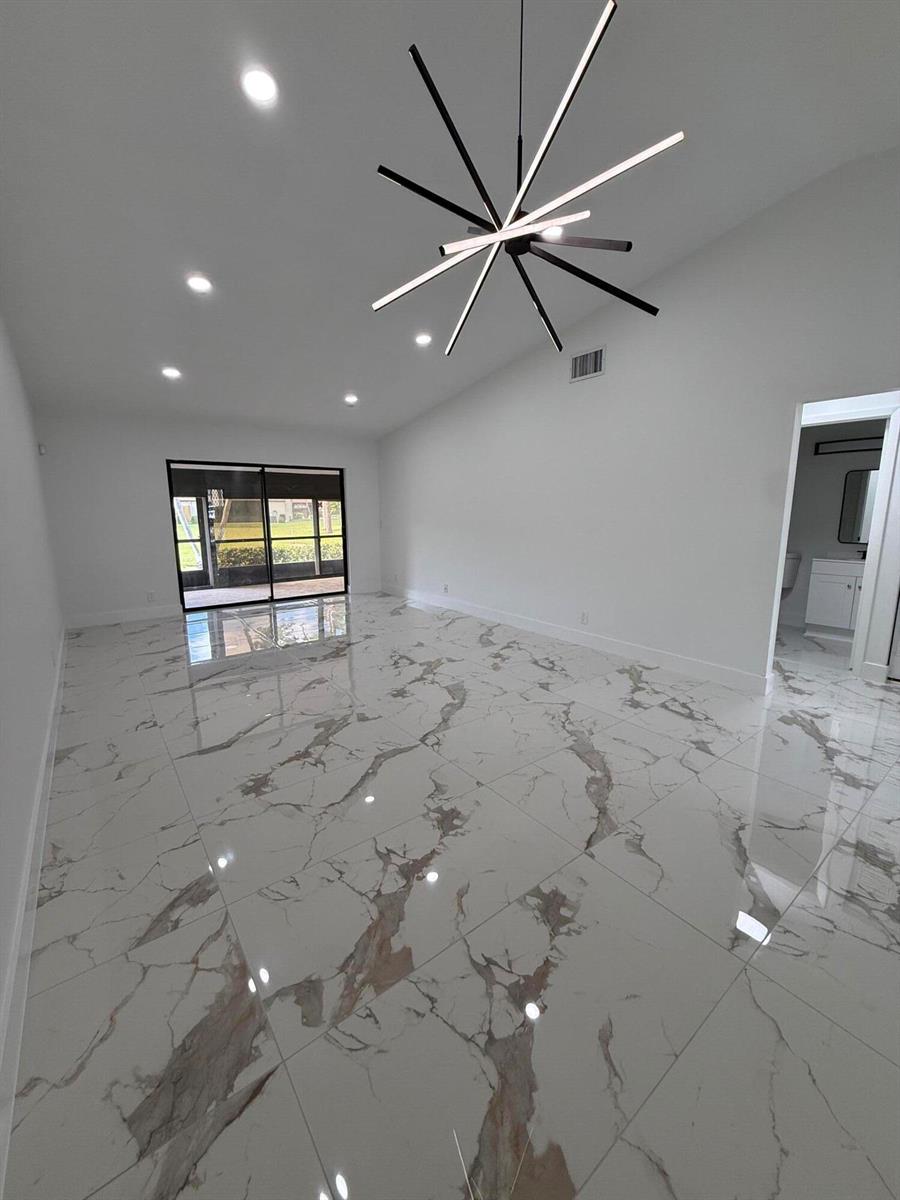 A bright room features white marble-look tile flooring, a modern starburst chandelier, and sliding doors — 817 Sky Pine Way # H, FL 33415, FL