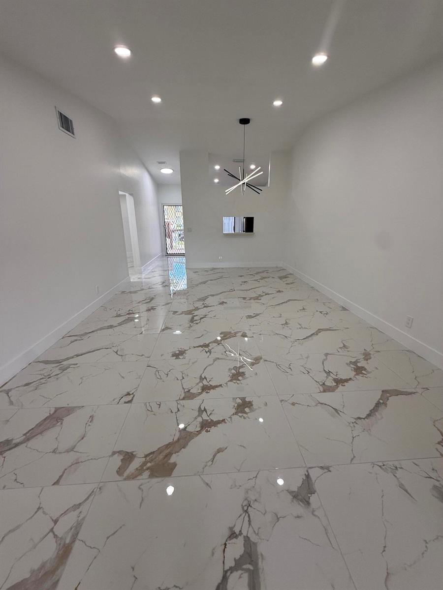 An empty room with white walls, recessed lighting, a modern chandelier, and marble-patterned tile flooring — 817 Sky Pine Way # H, FL 33415, FL