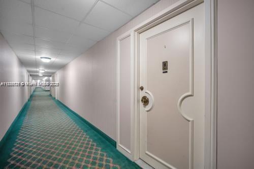 A long hallway with green patterned carpet leads to a white door with gold hardware — 1950 S Ocean Dr # 6K, Hallandale Beach FL 33009, HALLANDALE BEACH, FL
