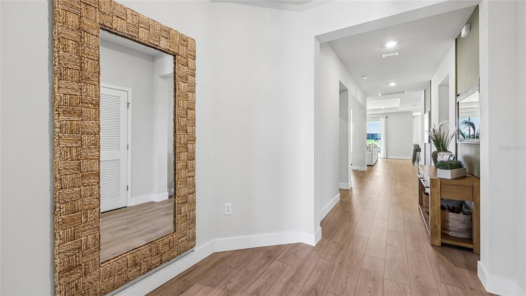 A bright hallway features light wood flooring, a large woven-frame mirror, and a wooden console — 12776 NW 17TH PLACE, NEWBERRY, FL