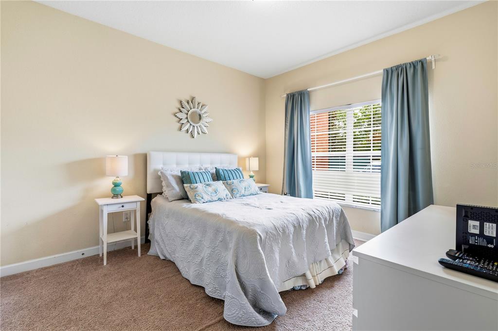 A bedroom features a bed with a white headboard, blue curtains, and beige carpeting — 2975 BANANA PALM DR DRIVE, KISSIMMEE, FL