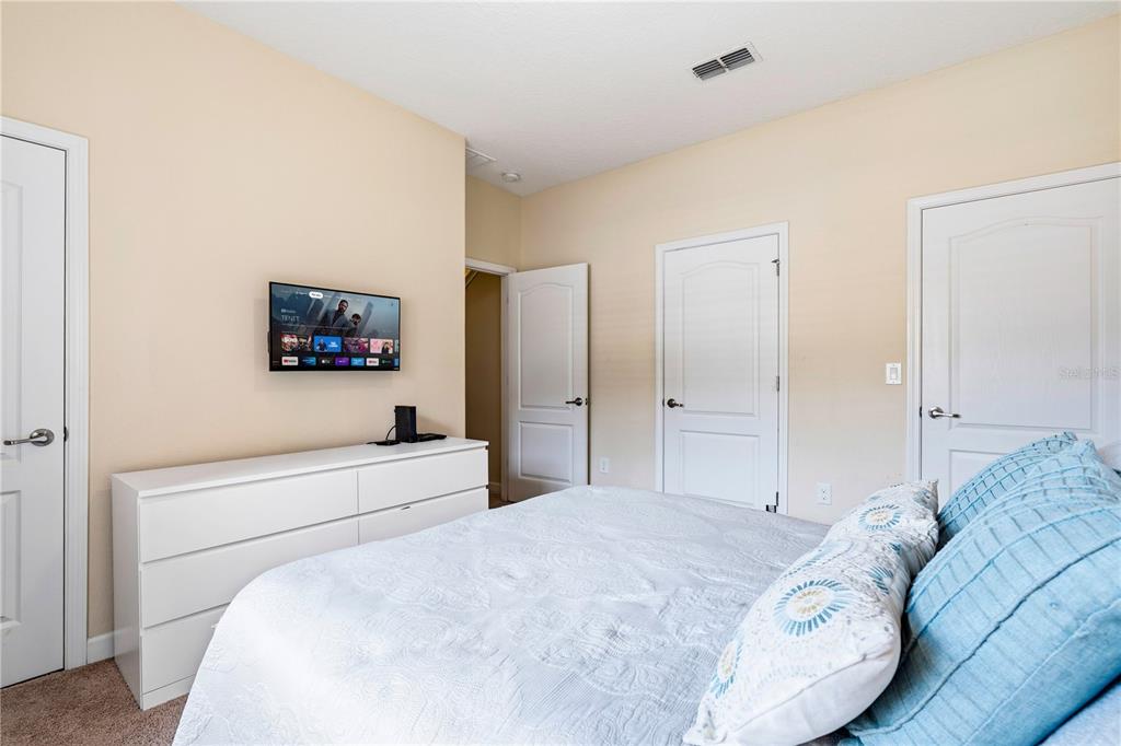 A bedroom features a white dresser, a wall-mounted television, and a bed with blue pillows — 2975 BANANA PALM DR DRIVE, KISSIMMEE, FL