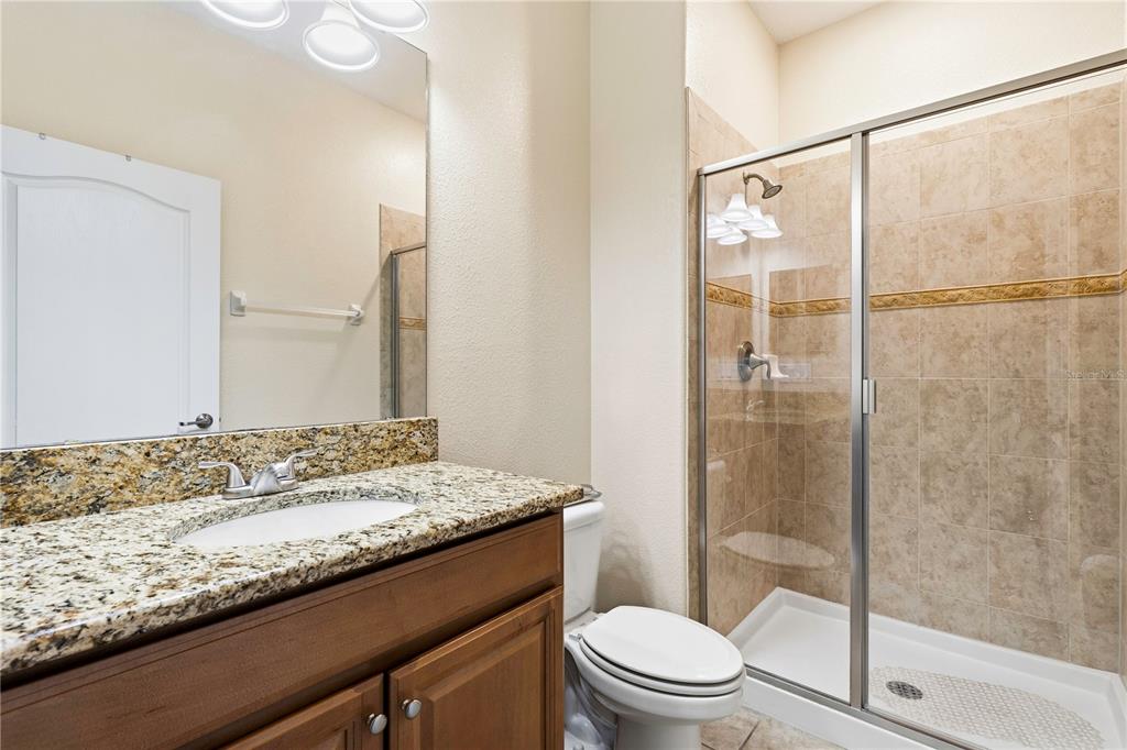 A bathroom features a granite vanity, a wooden cabinet, a toilet, and a glass-enclosed shower — 2975 BANANA PALM DR DRIVE, KISSIMMEE, FL