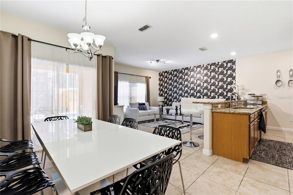 A dining area with a white table and black chairs opens to a kitchen and living room — 2975 BANANA PALM DR DRIVE, KISSIMMEE, FL