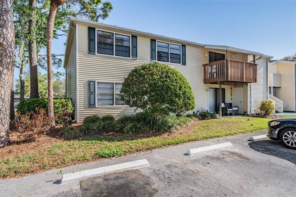 A two-story beige apartment building with a wooden balcony and a parking lot in front — 124 LOBLOLLY COURT UNIT H, OLDSMAR, FL