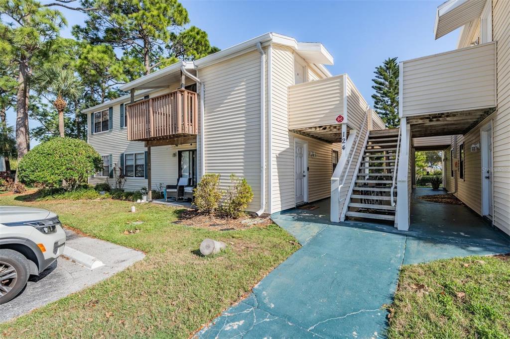 Exterior view of a two-story apartment building with beige siding, wooden balconies, and outdoor stairs — 124 LOBLOLLY COURT UNIT H, OLDSMAR, FL