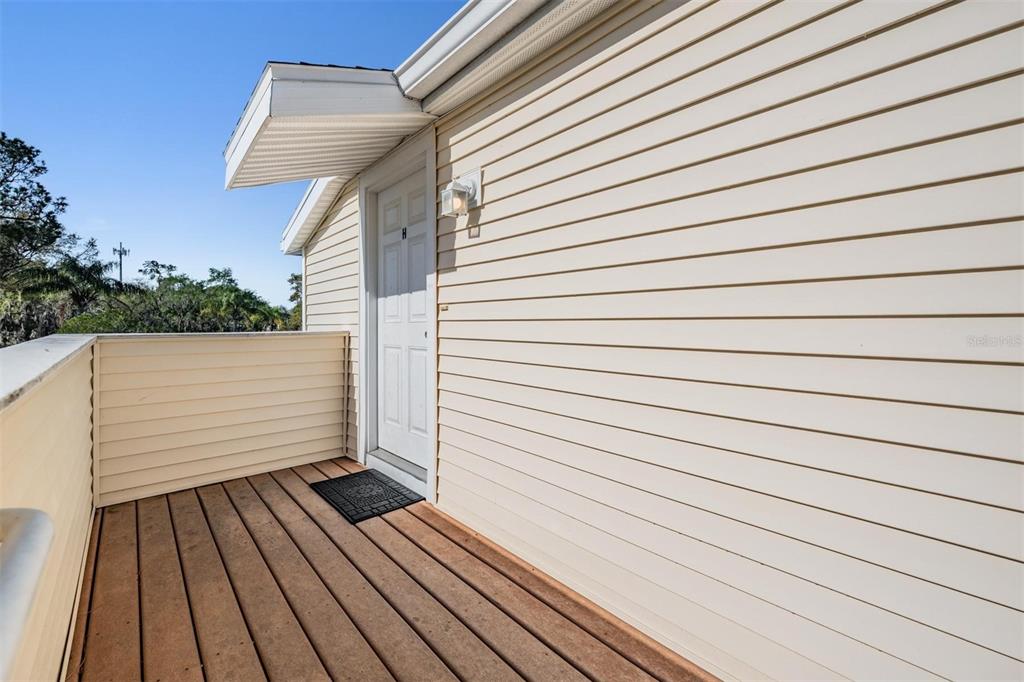 A wooden balcony with light-colored siding and a white door under a small overhang — 124 LOBLOLLY COURT UNIT H, OLDSMAR, FL