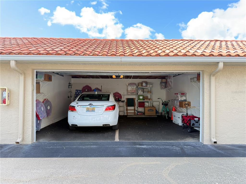 A white car is parked inside a single-car garage with storage shelves and a red wagon — 407 BOUCHELLE DRIVE UNIT 303, NEW SMYRNA BEACH, FL
