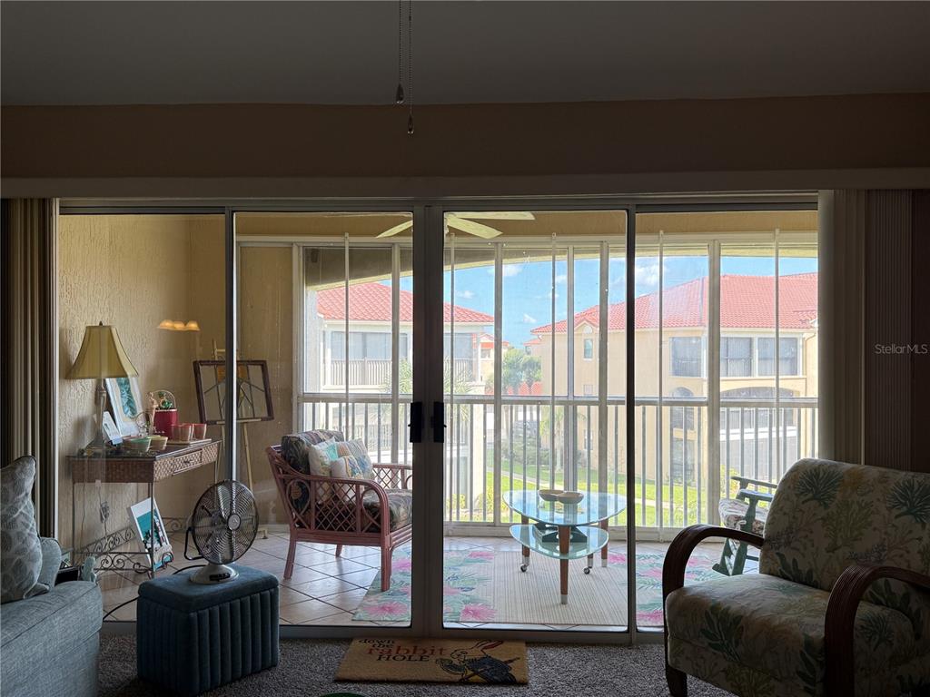 A living room looks out through sliding glass doors onto a screened-in balcony with outdoor furniture — 407 BOUCHELLE DRIVE UNIT 303, NEW SMYRNA BEACH, FL