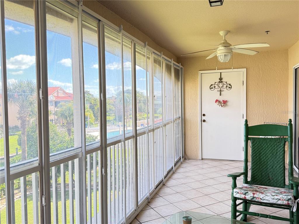 A screened-in balcony features tiled flooring, a ceiling fan, and a green rocking chair — 407 BOUCHELLE DRIVE UNIT 303, NEW SMYRNA BEACH, FL