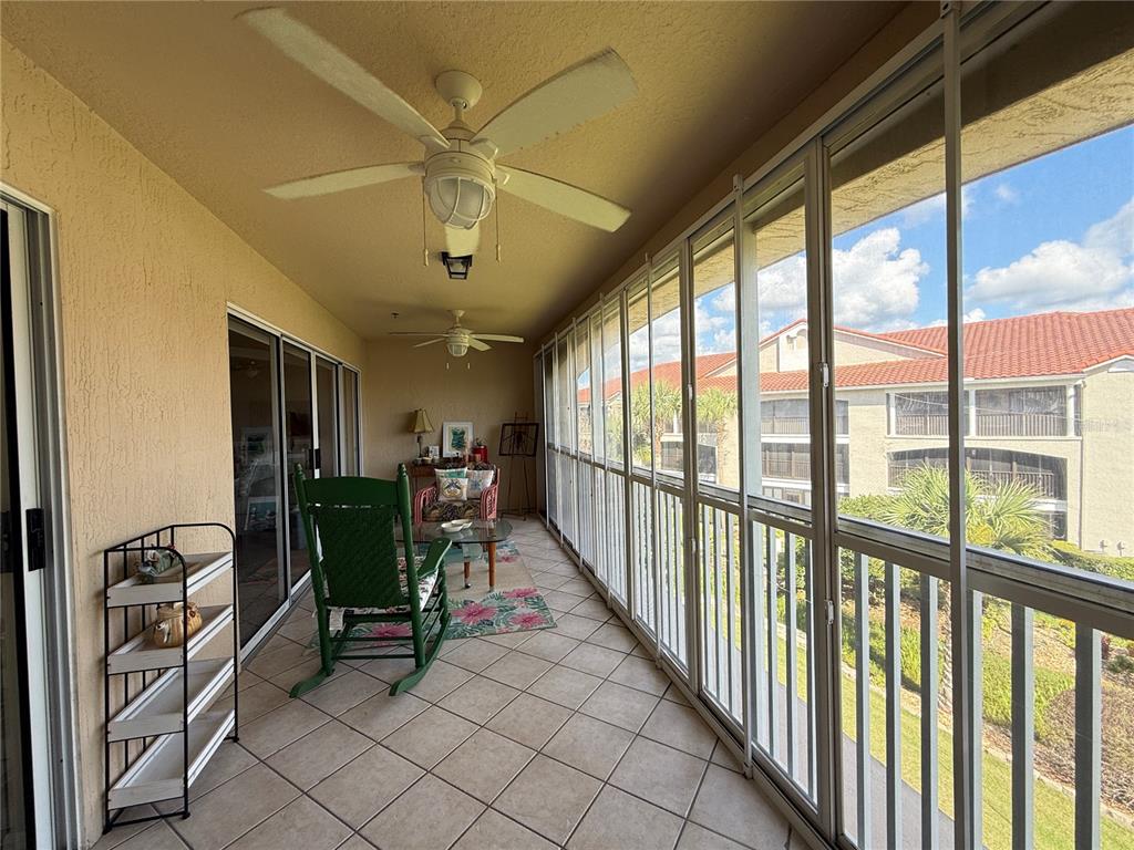 A tiled balcony features two ceiling fans, a green rocking chair, and floor-to-ceiling windows — 407 BOUCHELLE DRIVE UNIT 303, NEW SMYRNA BEACH, FL