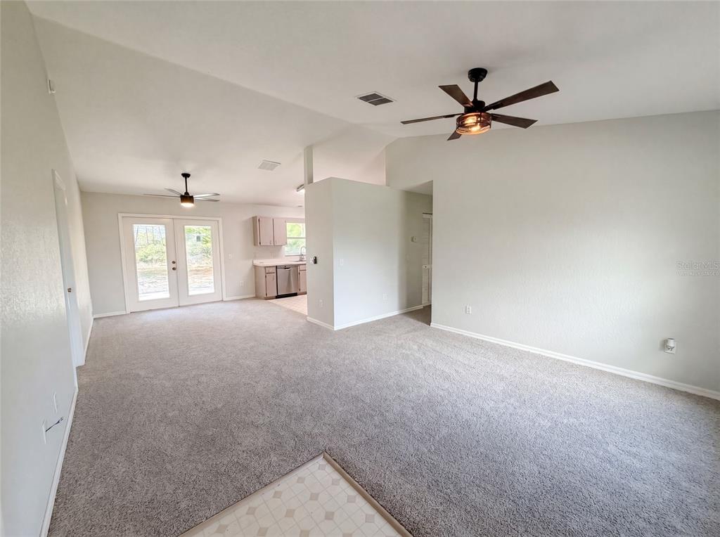 A carpeted living room with a ceiling fan opens to a kitchen with light cabinets — 17956 SW 25TH AVENUE ROAD, OCALA, FL