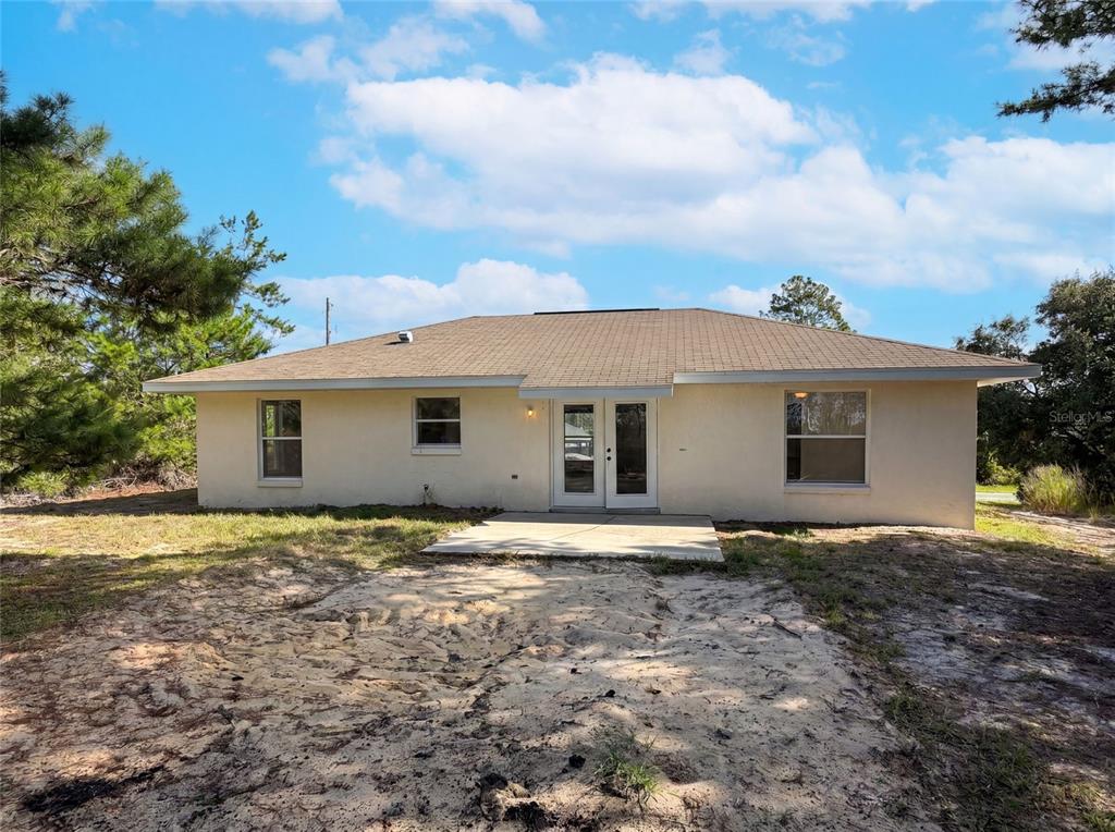 The rear exterior of a single-story house features a concrete patio and double glass doors — 17956 SW 25TH AVENUE ROAD, OCALA, FL