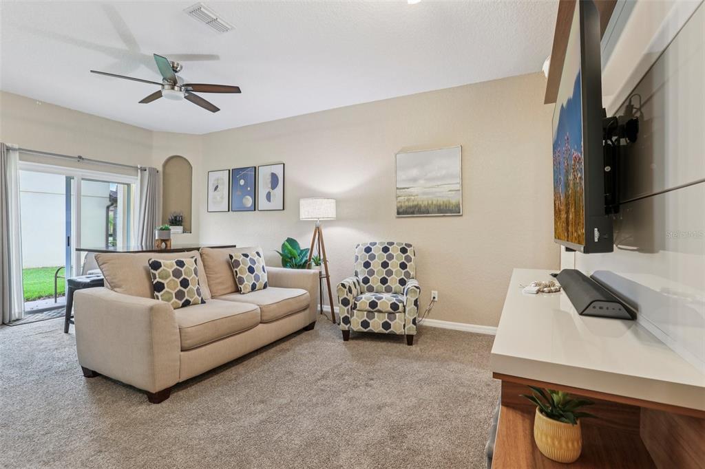 A living room features a beige sofa, patterned armchair, television, and sliding glass patio doors — 247 CALABRIA AVENUE, DAVENPORT, FL