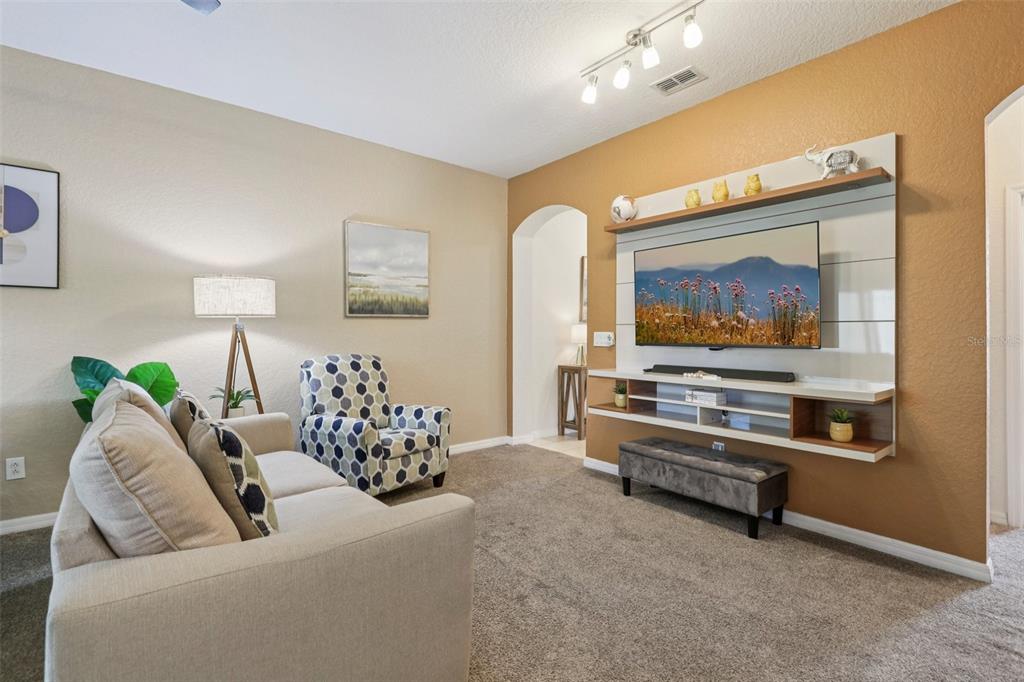 A living room features a tan sofa, a patterned armchair, and a wall-mounted television unit — 247 CALABRIA AVENUE, DAVENPORT, FL