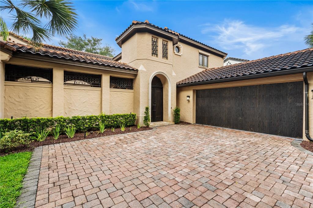 A beige stucco house with a tiled roof, arched entryway, and a paved driveway — 9841 COVENT GARDEN DRIVE, ORLANDO, FL