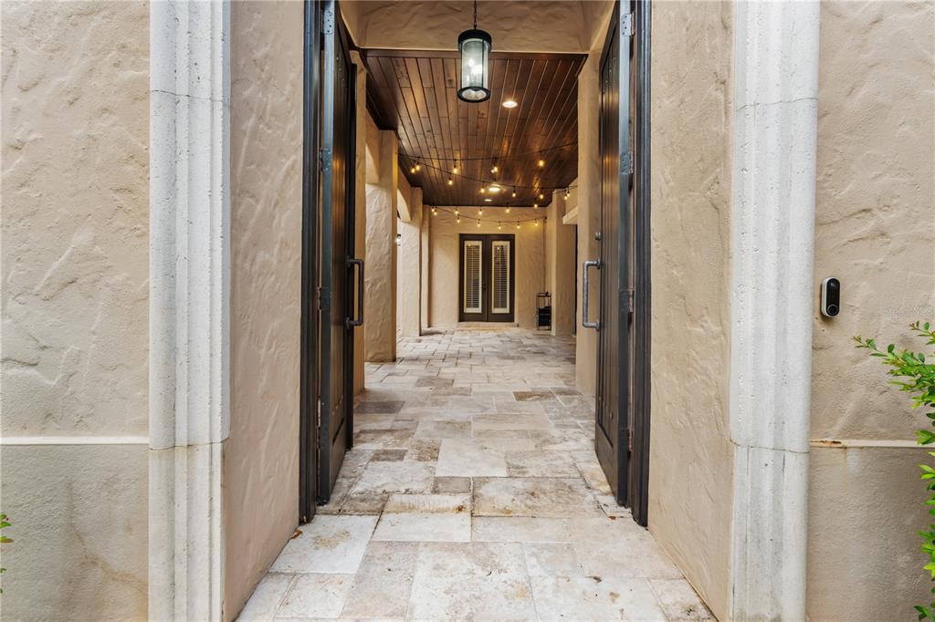 A stone-tiled entryway leads through open double doors to a covered patio with string lights — 9841 COVENT GARDEN DRIVE, ORLANDO, FL
