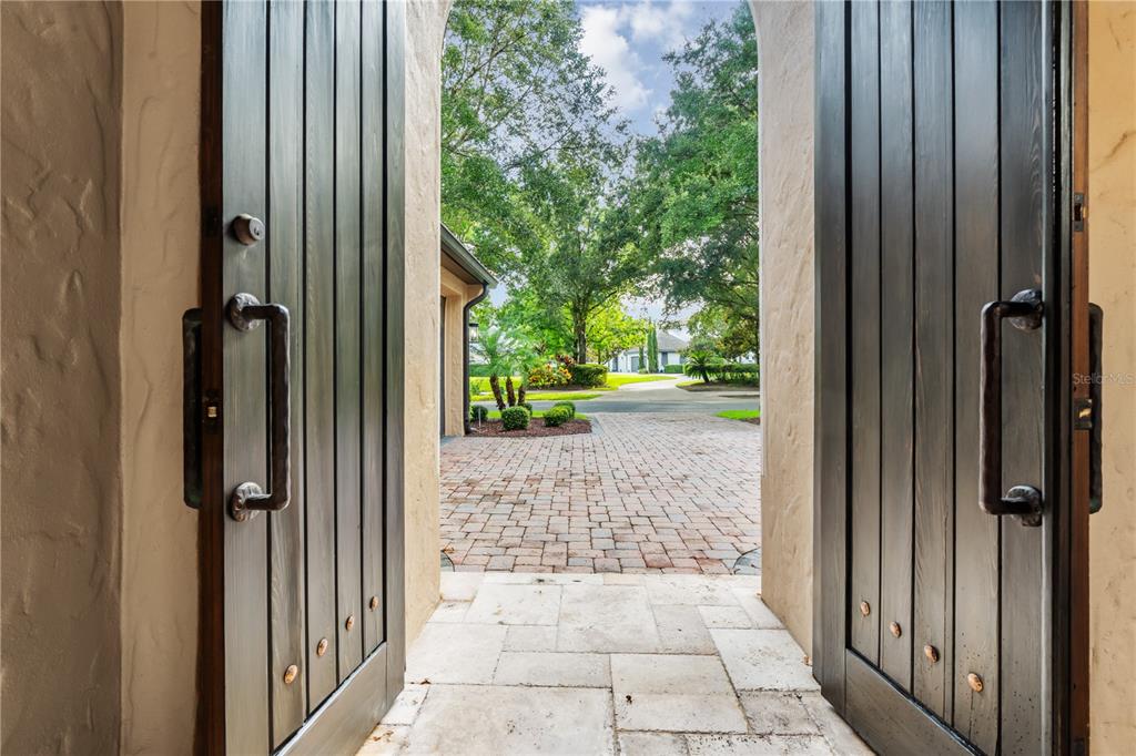 A view looking out through open dark wooden double doors onto a brick paved driveway — 9841 COVENT GARDEN DRIVE, ORLANDO, FL