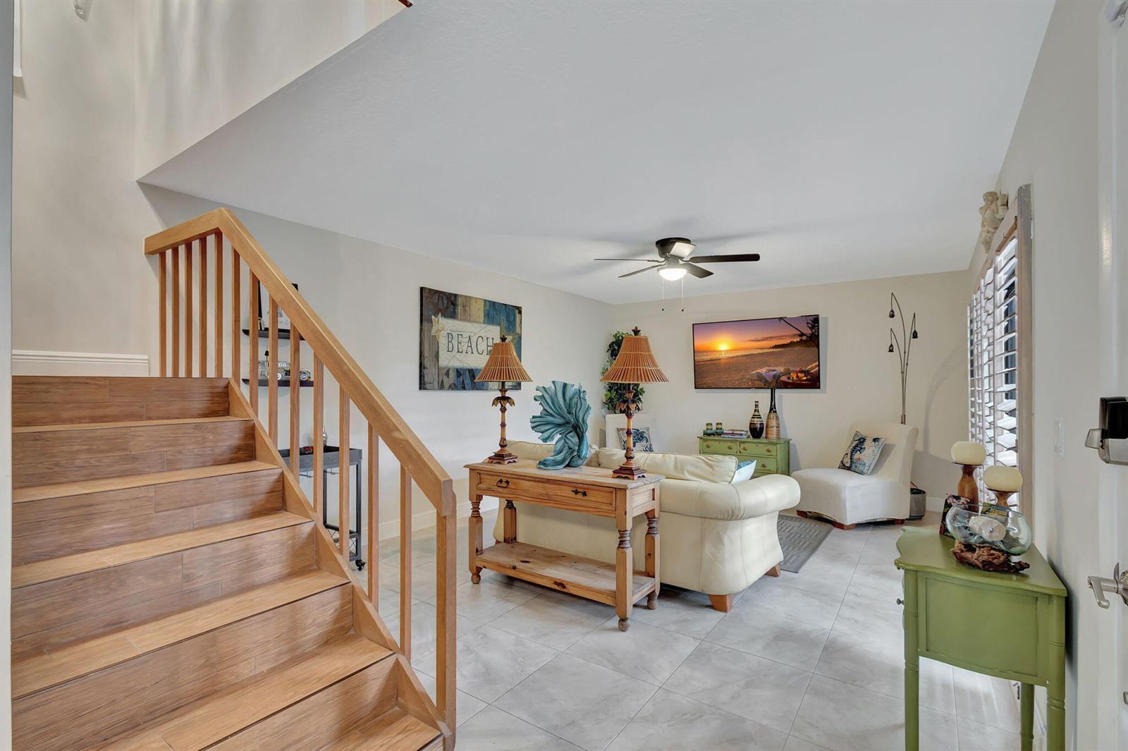 A living room features a wooden staircase, tile flooring, a beige sofa, and a television — 99 Lake Arbor Drive, Palm Springs FL 33461, PALM SPRINGS, FL