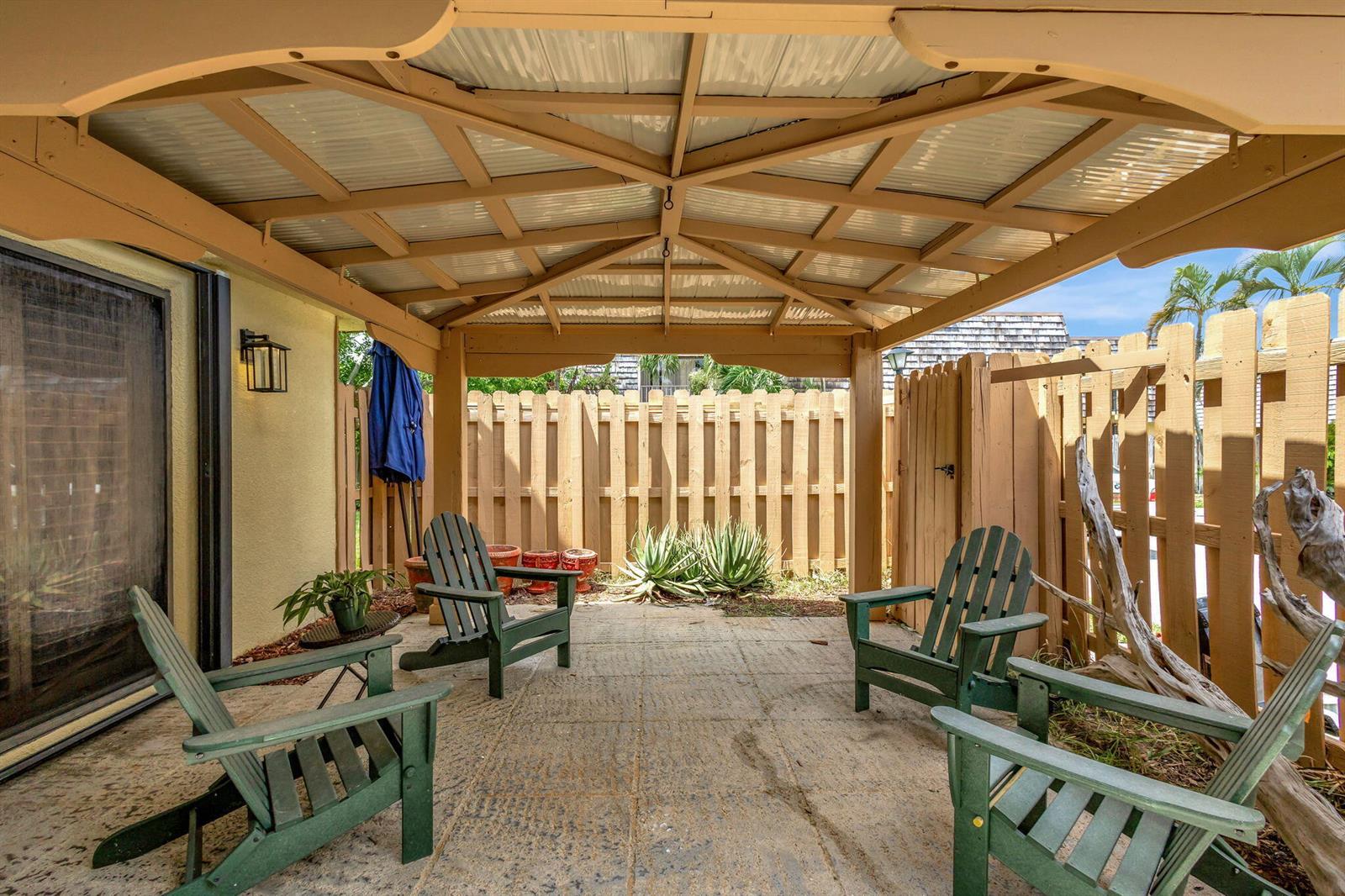 A covered patio features a concrete floor, four green Adirondack chairs, and a wooden fence — 99 Lake Arbor Drive, Palm Springs FL 33461, PALM SPRINGS, FL