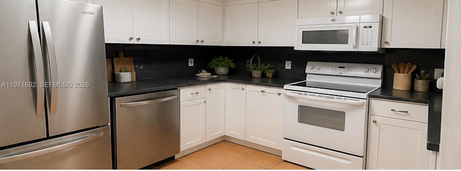 A kitchen features white cabinetry, black countertops, stainless steel appliances, and light-colored tile flooring — 9001 SW 94 ST # 113, Miami FL 33176, MIAMI, FL