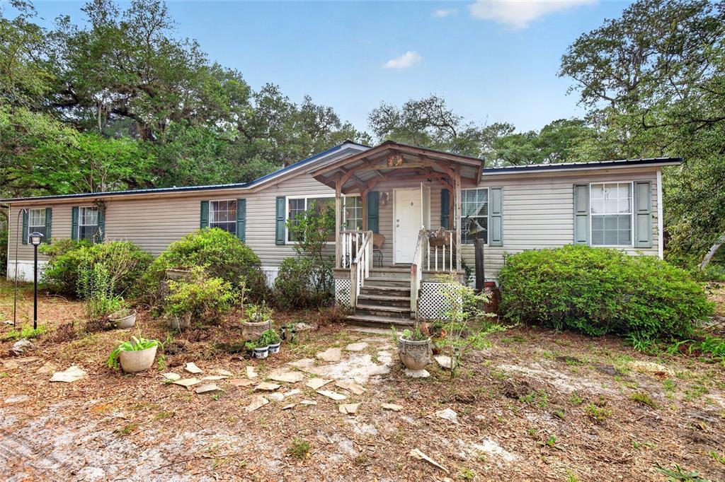 A single-story manufactured home with light gray siding and a wooden front porch entrance — 9190 NE 144TH TERRACE, SILVER SPRINGS, FL