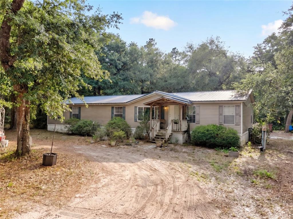A single-story manufactured home with a metal roof sits on a sandy, wooded lot — 9190 NE 144TH TERRACE, SILVER SPRINGS, FL