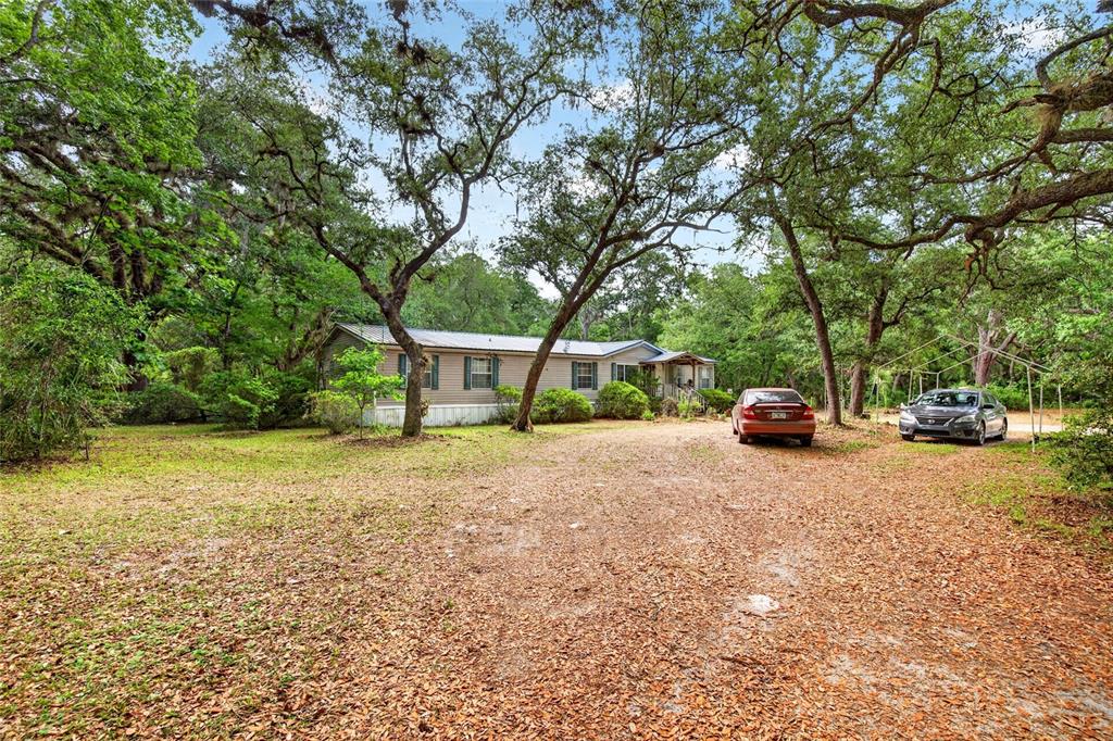 A single-story manufactured home sits on a wooded lot with two parked cars — 9190 NE 144TH TERRACE, SILVER SPRINGS, FL