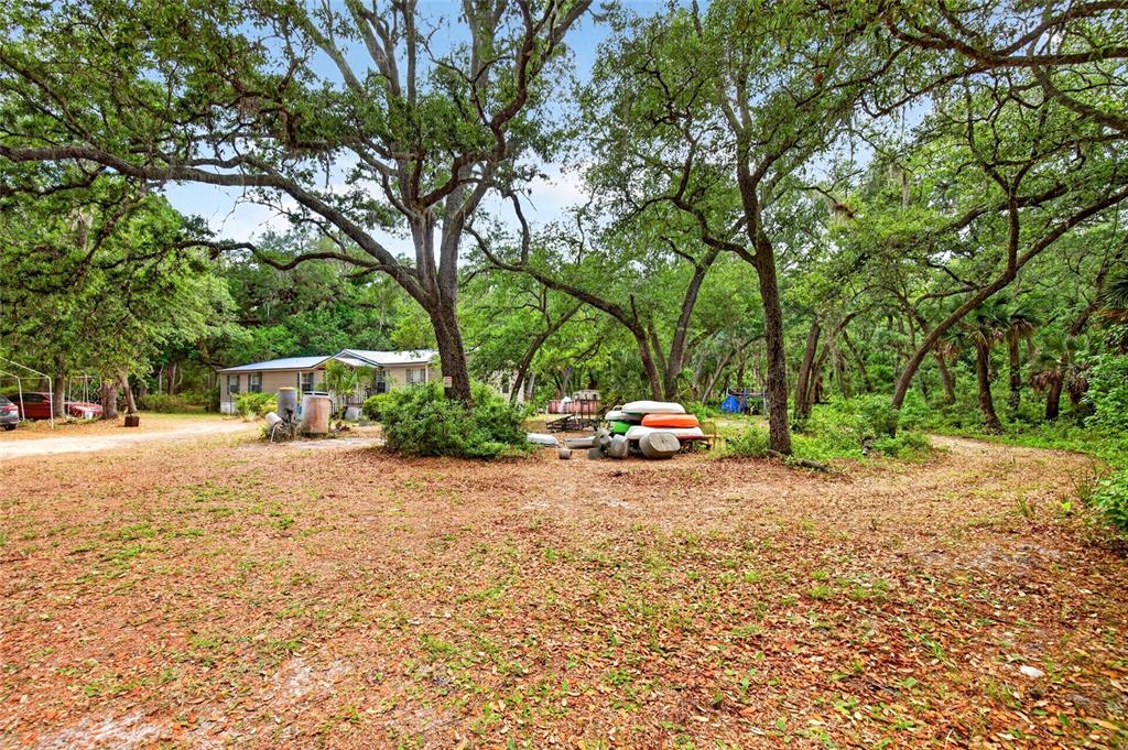 A mobile home sits on a wooded lot with scattered kayaks and outdoor equipment — 9190 NE 144TH TERRACE, SILVER SPRINGS, FL
